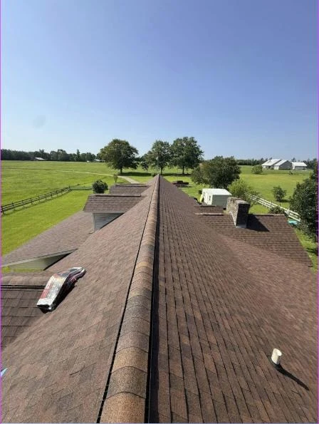 Finished architectural shingle roof ridge overlooking open pasture and fencing